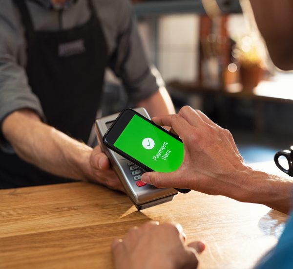 Customer paying bill through smartphone using NFC technology. Closeup of hand making payment through contactless machine. Woman hand holding mobile phone with green screen and paying the bill with contact less technology.