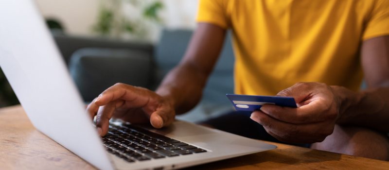Unrecognisable African American man using laptop and credit card to buy things online. E-commerce concept.
